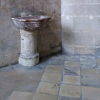 Old sandstone floor, wall, and column frame a timeworn marble font.